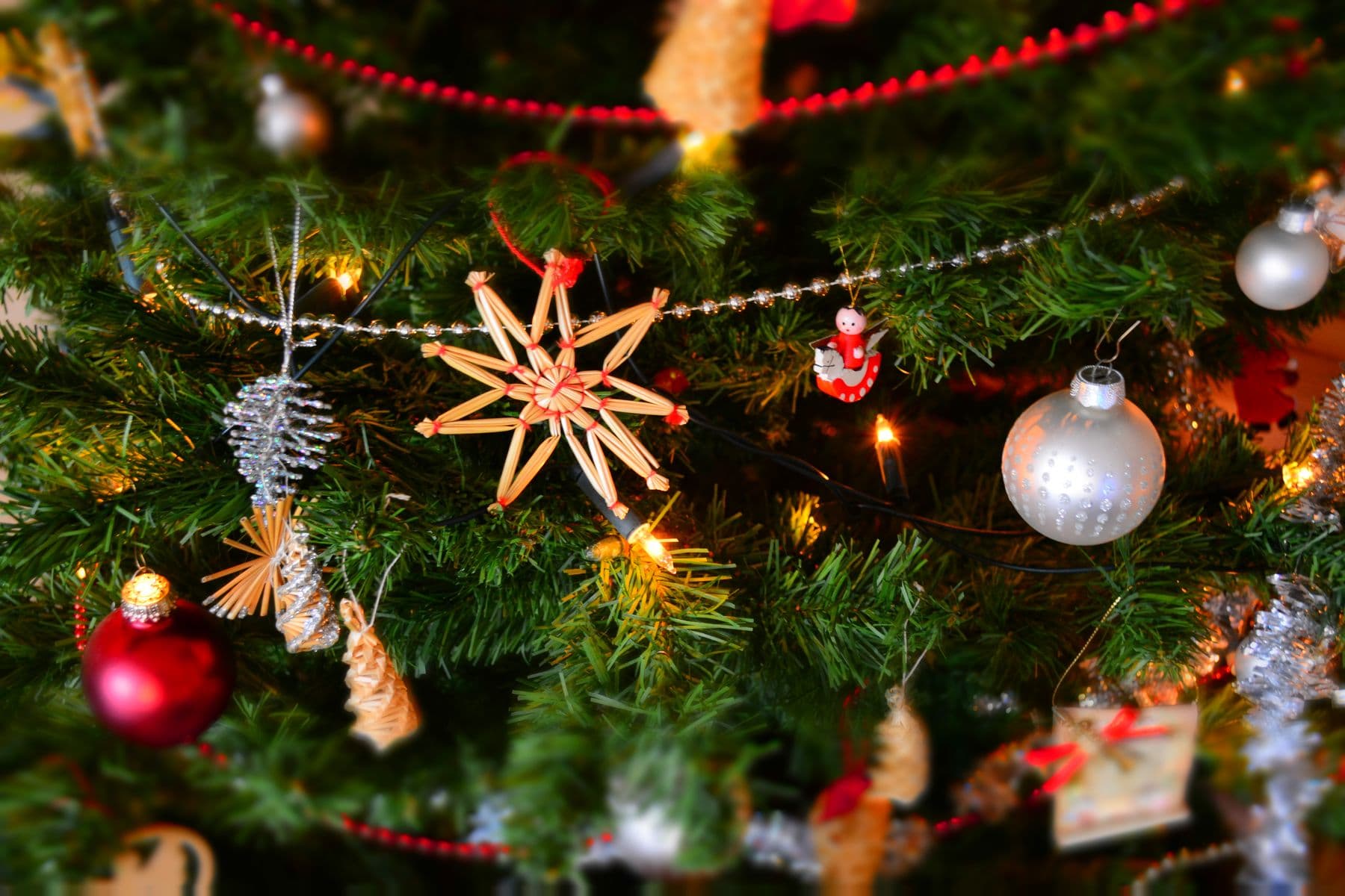 Christmas ornaments and a straw star hanging on an evergreen tree with warm lights